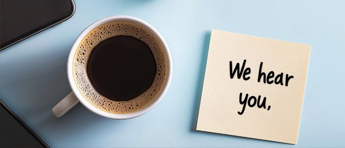a notepad with we hear you written on it, placed next to a cup of coffee