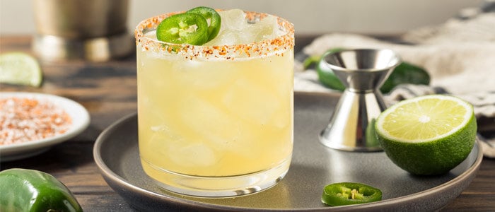 a spicy margarita garnished with lime and jalapenos, served in a glass with a salted rim