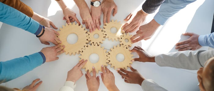 hands touching cogs in team building exercise